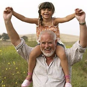 Older man with beard with his granddaughter on his shoulders laughing